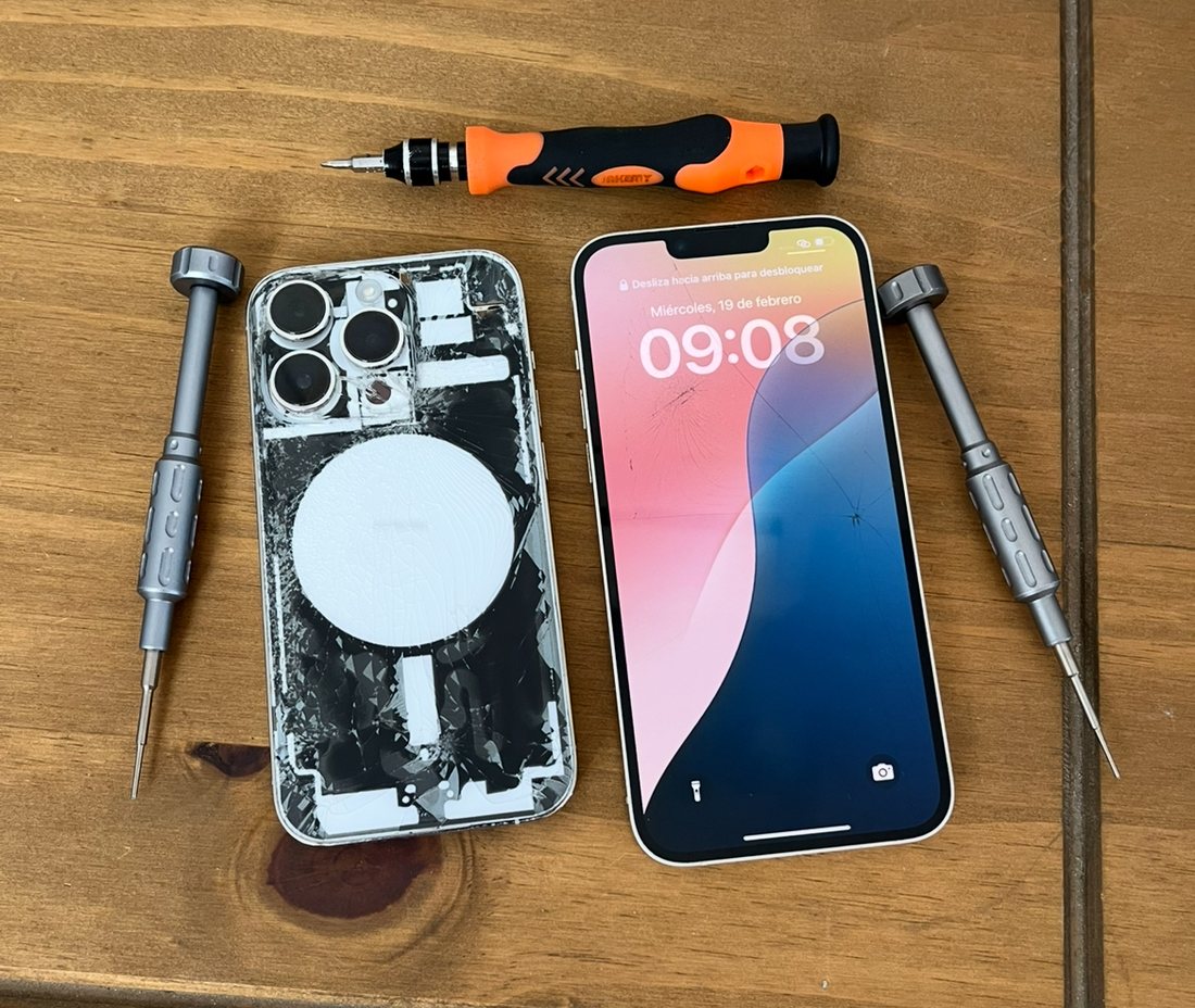 iPhone con la tapa trasera rota, junto a otro equipo y destornilladores